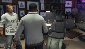 Скриншот из GTA 5: интерьер тату-салона, слева персонаж в белой футболке с цветной татуировкой на предплечье, в центре клиент спиной к камере, на заднем плане кресло тату-мастера, лампа, полки с красками и стены с эскизами татуировок