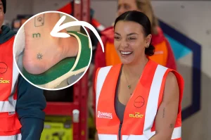 Улыбающаяся Тайла из The Block в оранжевом жилете Bunnings Warehouse; в круглой врезке крупным планом лодыжка со свежей татуировкой логотипа Domain, буквой m и символом солнца, на которую указывает белая стрелка