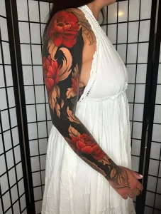 Полная рука (full sleeve) с цветной татуировкой: крупные красные пионы и золотисто-бежевые листья на плотном чёрном фоне, женщина в белом платье на фоне японского шoji-экрана