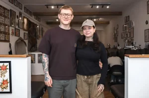 Супруги-тату-мастера Thomas и Rhiannon Goldsmith позируют в интерьере своей новой студии Til Death Tattoo в Сандерленде; на предплечье мужчины видна цветная татуировка в традиционном стиле, на стенах — галерея эскизов и работ