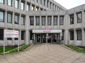 Бетонный фасад Solford Civic Centre в Солфорде (Большой Манчестер) с вращающимися входными дверями, розовым логотипом Solford City Council и указателем направлений; здание муниципального совета, связанного со скандалом в детском доме