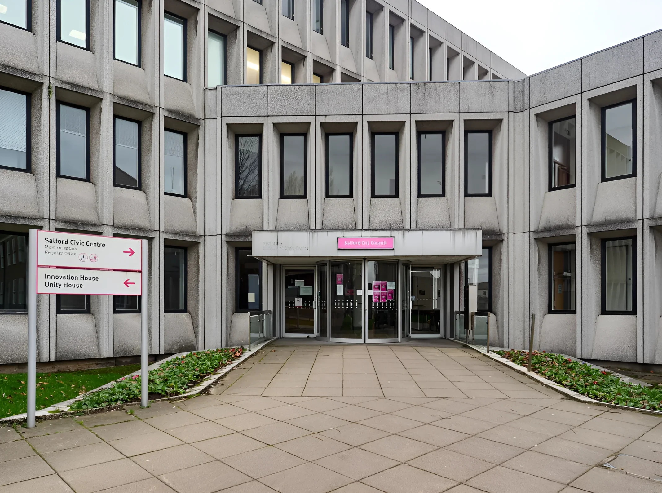 Бетонный фасад Solford Civic Centre в Солфорде (Большой Манчестер) с вращающимися входными дверями, розовым логотипом Solford City Council и указателем направлений; здание муниципального совета, связанного со скандалом в детском доме