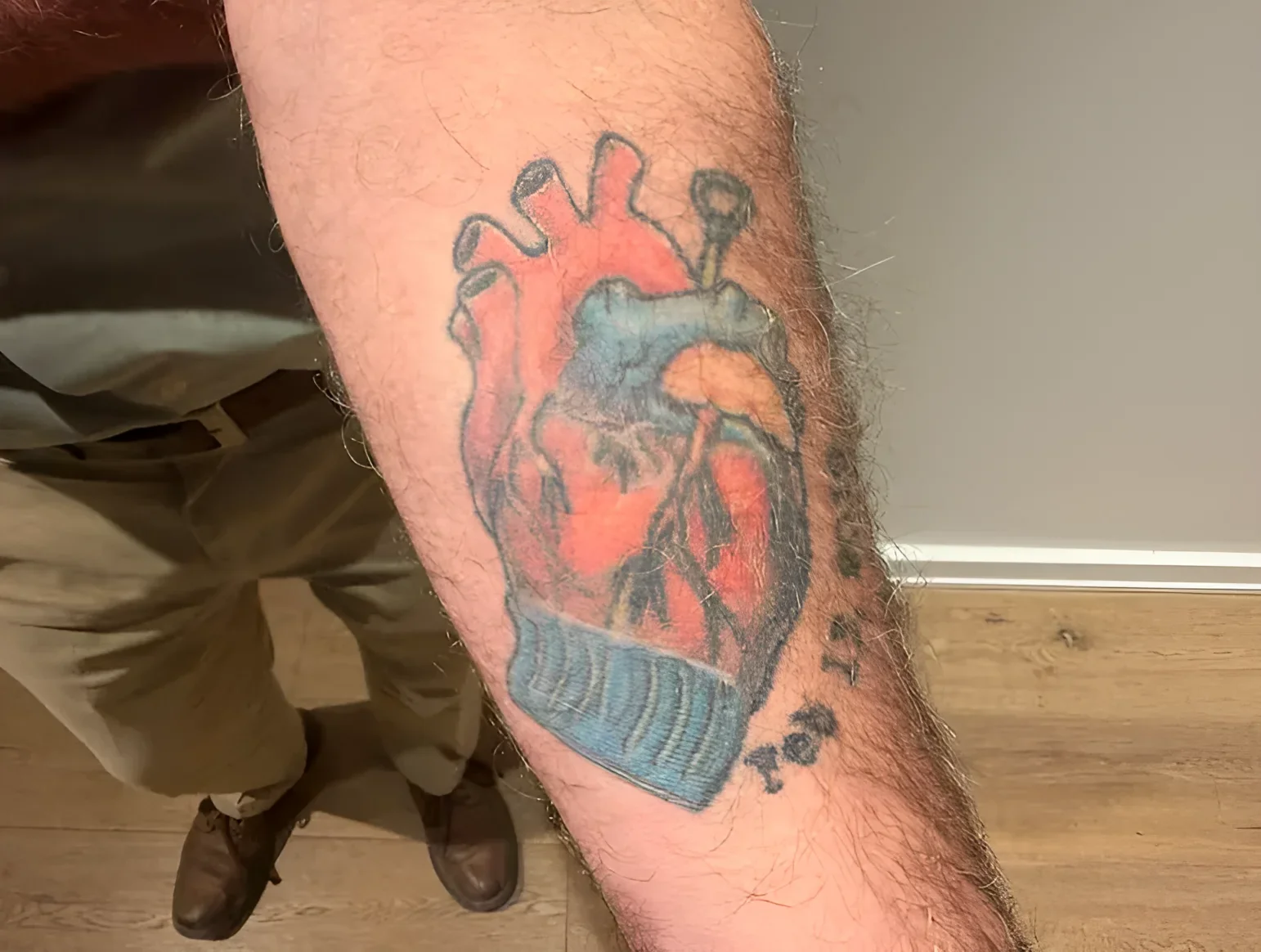 Крупный план предплечья с цветной татуировкой анатомического сердца в традиционном стиле и надписью с датой рядом