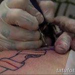 Фото тату процесса нанесения рисунка на руку. Мастер в голубых перчатках работает тату-машинкой над эскизом татуировки.
