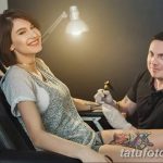 Фото тату процесса нанесения рисунка на ногу. Девушка улыбается, а мастер делает татуировку на ее ноге.