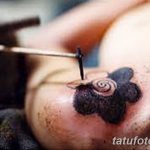 Фото процесса нанесения татуировки. Видна рука мастера с тату-машинкой и кожа клиента, на которую наносится черный узор.
