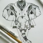 Черно-белый эскиз татуировки головы слона, украшенной мандалой и геометрическими узорами. Рисунок выполнен в детальной технике с использованием штриховки.